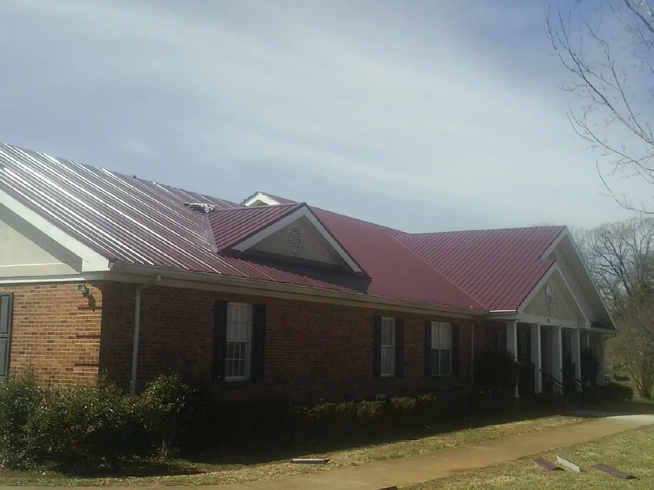 Red metal roof with gabled entries on a long brick building, from a Hail Damage Roof Repair job in Sumterville