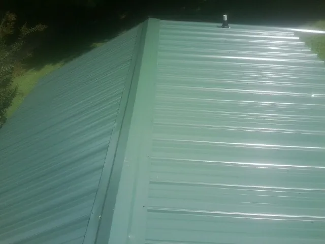 New green metal panels meeting at the ridge of a roof — Flat Roof Repair work by our crew in Sumterville