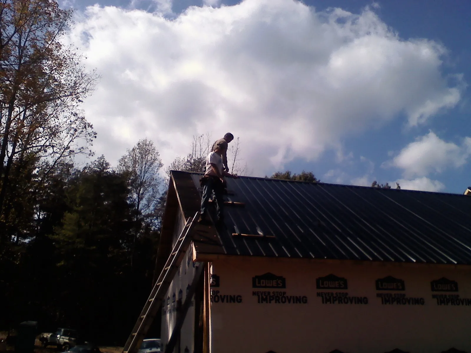 Roofer fastening dark metal panels high against a cloudy sky, from a Roof Inspection job in Sumterville