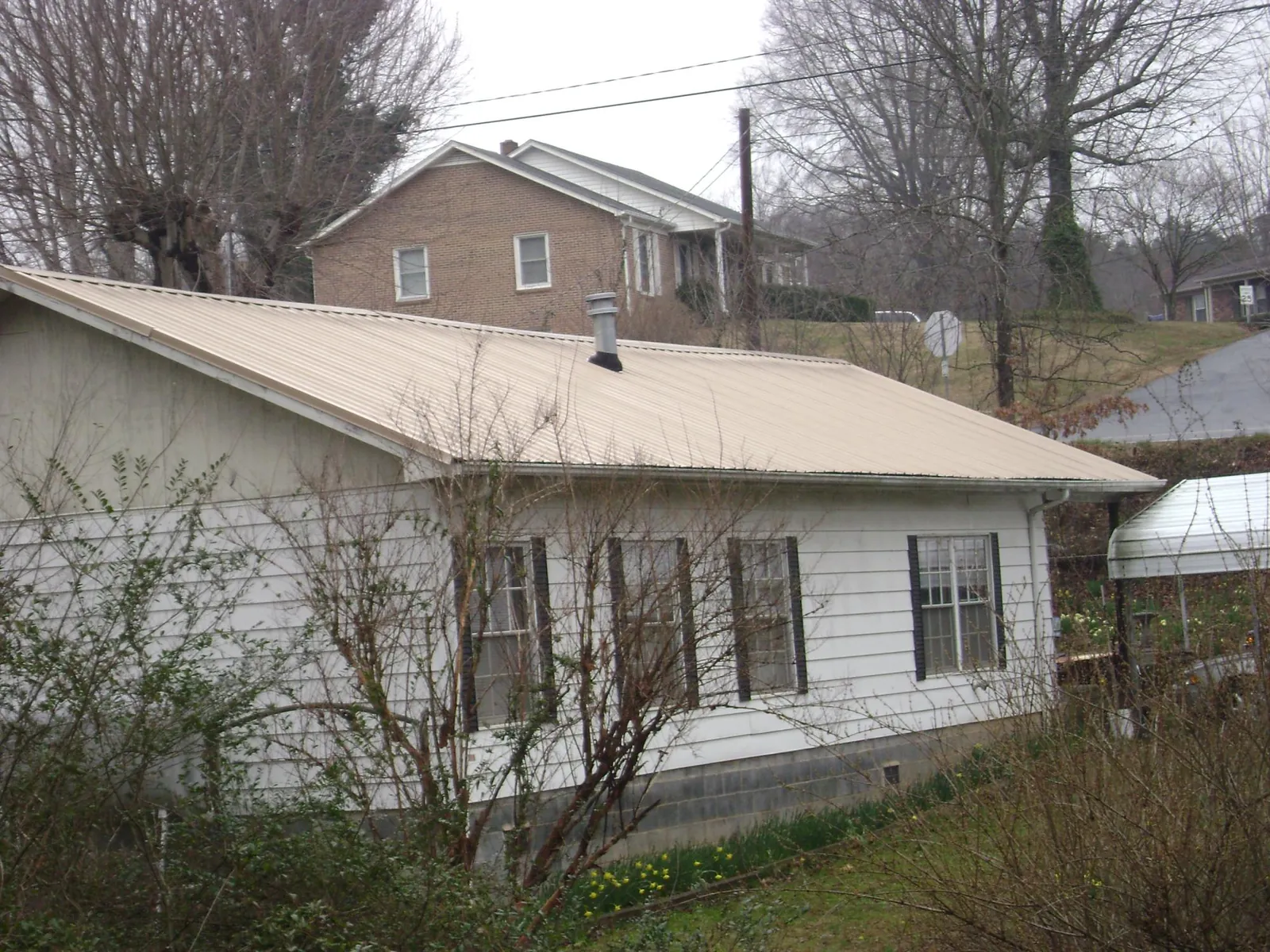 Tan metal roof on a white sided house set into a hillside — Commercial Roofing by Roofing Brothers in Sumterville