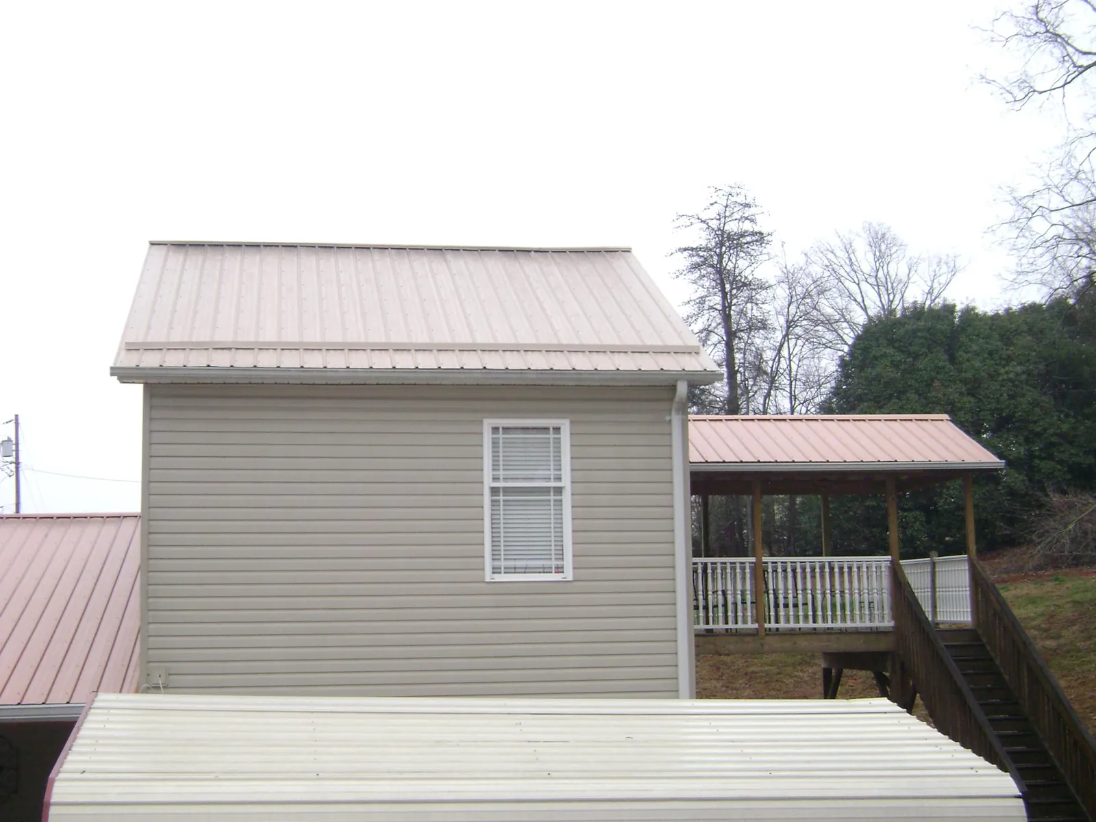 Tan metal roofs on a two story addition and attached porch, from a Roof Replacement job in Sumterville